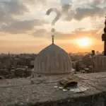 Ilustrasi siluet muadzin memandang kubah masjid saat senja dengan awan berbentuk tanda tanya, serta tumpukan uang koin di atas dinding batu, menggambarkan pembahasan hukum menggaji muadzin dalam Islam.