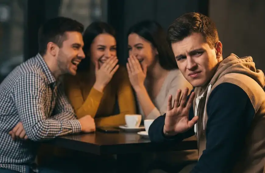 Home 15 Ilustrasi seorang pria/wanita yang menunjukkan ekspresi tidak nyaman dan memberi isyarat tangan menolak saat teman-temannya sedang asyik tertawa menggunjing orang lain.