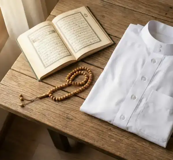 Home 5 Baju koko putih bersih terlipat rapi di samping kitab doa Al-Qur'an terbuka dan tasbih kayu di atas meja kayu dengan cahaya matahari pagi.