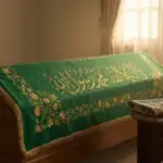 Panduan Lengkap Tata Cara Merawat Jenazah: Sebuah keranda jenazah kayu yang ditutupi kain hijau bersulam kaligrafi emas "Laa ilaha illallah Muhammad Rasulullah", diletakkan di ruangan yang tenang dengan cahaya matahari lembut, melambangkan tajhizul jenazah.
