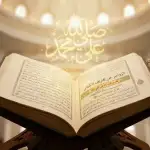 A photograph of the antique book **Al-Zawājir ʿan Iqtirāf al-Kabāʾir** by **Ibn Hajar al-Haytami**, opened on a wooden *rehal* inside a mosque. Radiant golden Arabic calligraphy reading **“Ṣallā Allāhu ʿalā Muḥammad”** rises from the pages, symbolizing the blessings and spiritual light of sending ṣalawāt upon the Prophet.