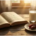 An open antique Islamic manuscript next to a glass of milk, a glass of water, and three dates on a wooden table at sunset.