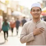 A Muslim man smiling patiently, placing his hand on his chest as a symbol of restraining his anger and saying 'Inni Saim' (I am fasting).