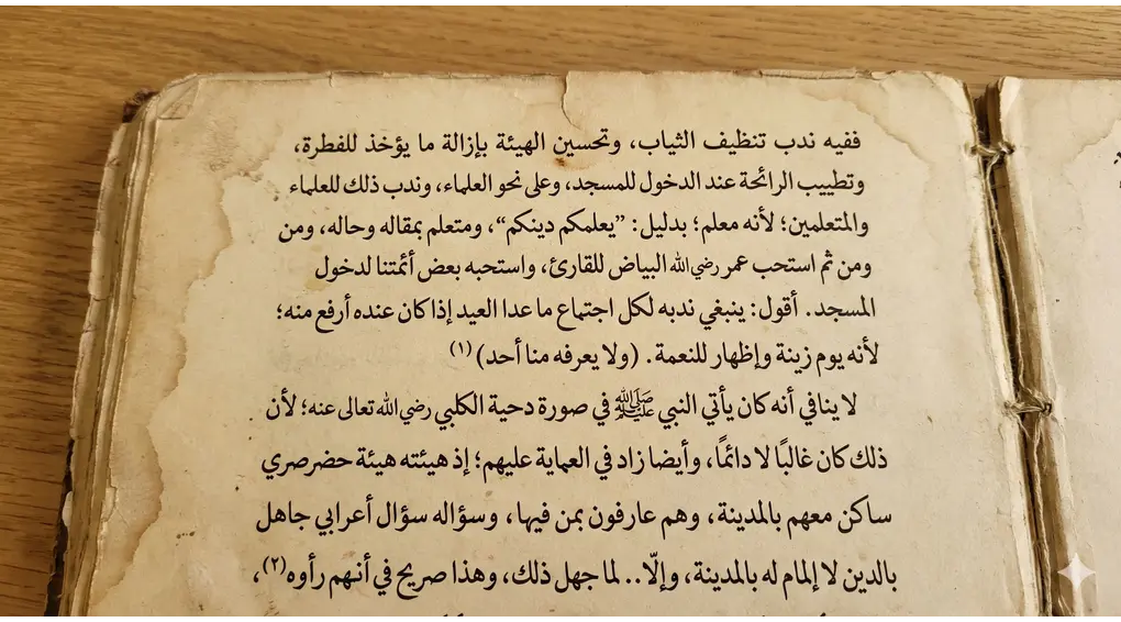Pakaian Penuntut Ilmu: Sunnah Putih, Bersih & Wangi (Kajian Hadits Jibril) 2 Halaman terbuka dari kitab kuning klasik Al-Fath Al-Mubin bertuliskan huruf Arab gundul sebagai rujukan istinbath hukum fikih tentang adab pakaian.