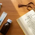 Do Injections & Ear Drops Break Fasting? A Shafi'i Medical Guide A flat lay view on a wooden table, showing a stethoscope, a sterile syringe, a small brown medicine bottle, an open Arabic Fiqh book (Asna al-Matalib), and a string of prayer bead tasbih.