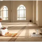 Foto interior masjid yang terang menunjukkan dua pria Muslim; satu sedang khusyuk membaca Al-Qur'an, dan yang lainnya sedang menulis catatan dan makan ringan dengan tenang di sudut lain. Ini menggambarkan keseimbangan antara ibadah mahdhah dan aktivitas mubah yang diperbolehkan saat i'tikaf.