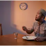 Seorang pria Muslim dengan ekspresi terkejut melihat jam dinding sambil memegang sendok makan, ilustrasi lupa makan saat puasa.Seorang pria Muslim dengan ekspresi terkejut melihat jam dinding sambil memegang sendok makan, ilustrasi lupa makan saat puasa.