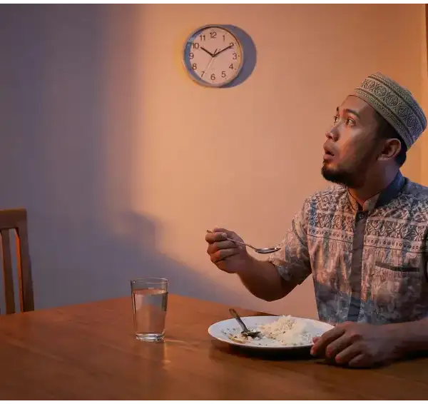 Seorang pria Muslim dengan ekspresi terkejut melihat jam dinding sambil memegang sendok makan, ilustrasi lupa makan saat puasa.Seorang pria Muslim dengan ekspresi terkejut melihat jam dinding sambil memegang sendok makan, ilustrasi lupa makan saat puasa.