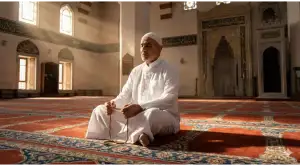Home 7 A Muslim man sitting devoutly in a sunlit mosque, symbolizing the solemn intention of making an i'tikaf nadhr (vow).