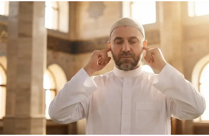 A medium close-up photo of a Muslim muadhin in a mosque, calling the Adhan with a focused expression and placing his index fingers in his ears according to the Sunnah.