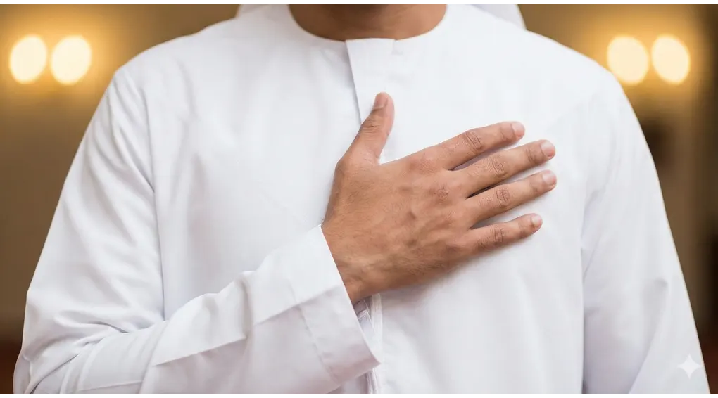 Rukun Mandi Wajib: 2 Syarat Sah yang Tidak Boleh Ditinggalkan (Fikih Syafi'i) 2 Close-up pria Muslim berbaju putih meletakkan tangan kanan di dada kiri, melambangkan niat yang bertempat di dalam hati.