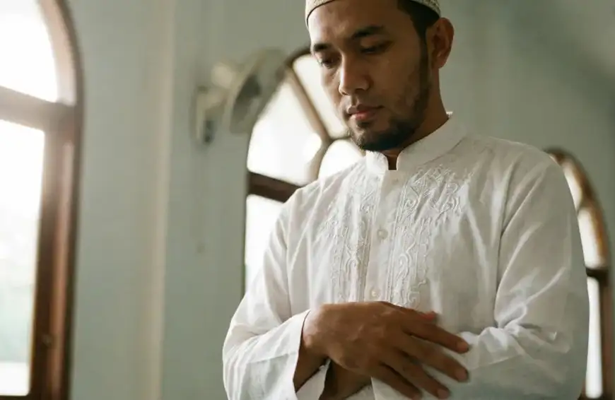 A Muslim standing humbly with folded hands, showing the correct posture while reciting the Iftitah prayer during Salah.