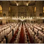 Ribuan jamaah pria berbaris rapi melaksanakan shalat Tarawih berjamaah di dalam interior masjid agung yang megah dengan cahaya keemasan pada malam Ramadhan.