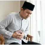 vomit while fasting: Neatly dressed Muslim man holding his stomach, feeling nauseous while fasting during the day.