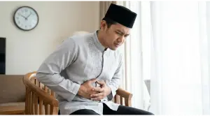Home 5 vomit while fasting: Neatly dressed Muslim man holding his stomach, feeling nauseous while fasting during the day.