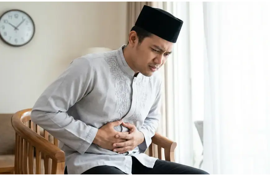 vomit while fasting: Neatly dressed Muslim man holding his stomach, feeling nauseous while fasting during the day.