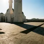 Halaman masjid di siang hari yang terik dengan bayangan dinding yang memanjang — ilustrasi kondisi ibrad shalat Dzuhur