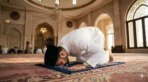 Pria Muslim memakai baju koko putih dan peci bersujud khusyuk saat melaksanakan ibadah shalat fardhu di atas sajadah masjid