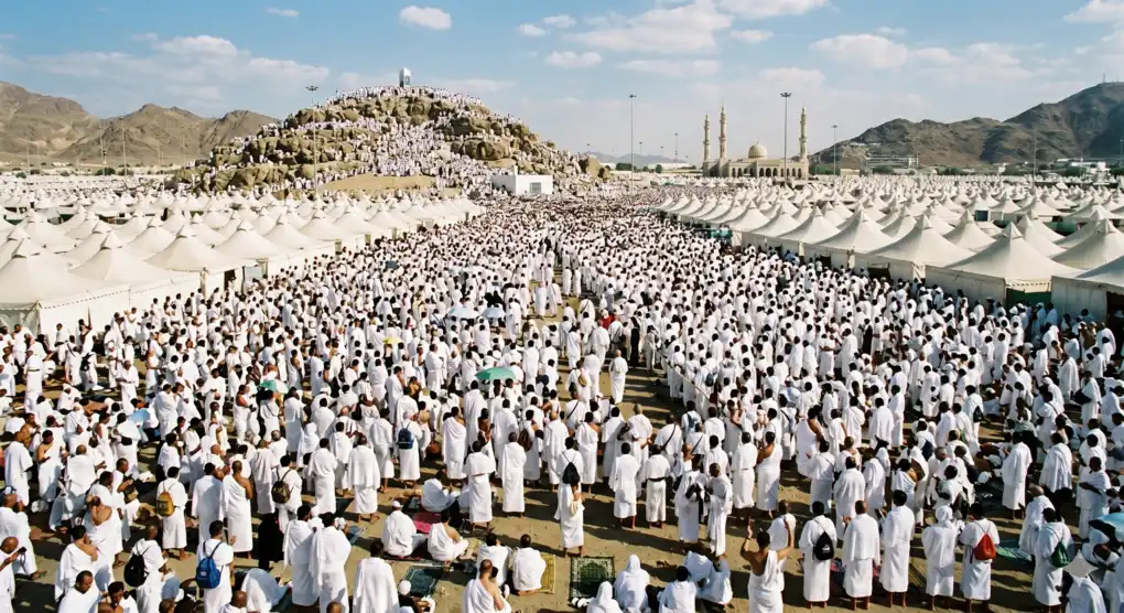 Foto pemandangan luas Padang Arafah yang dipenuhi jutaan jamaah haji berpakaian ihram putih sedang melaksanakan rukun wukuf, dengan latar belakang bukit berbatu dan tenda-tenda jamaah.