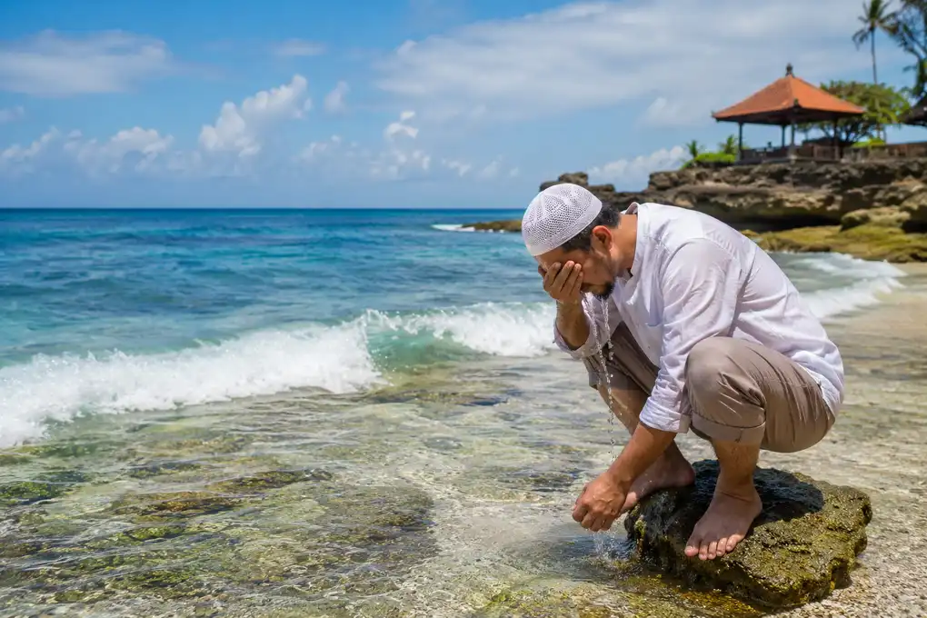 Muslim performing wudu by the sea using seawater for purification