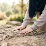 Close-up makro tangan seorang wanita Muslim berhijab menepuk permukaan batu alam yang bertekstur dengan lembut, mengumpulkan debu murni untuk melakukan tayammum, dengan latar belakang alam yang menenangkan.